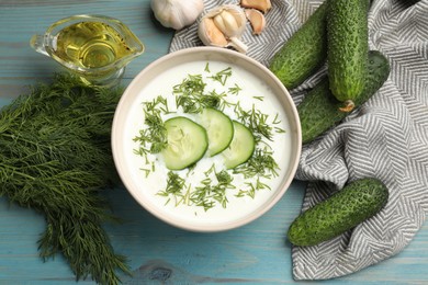 Photo of Tasty cucumber soup in bowl and ingredients on light blue wooden table, flat lay