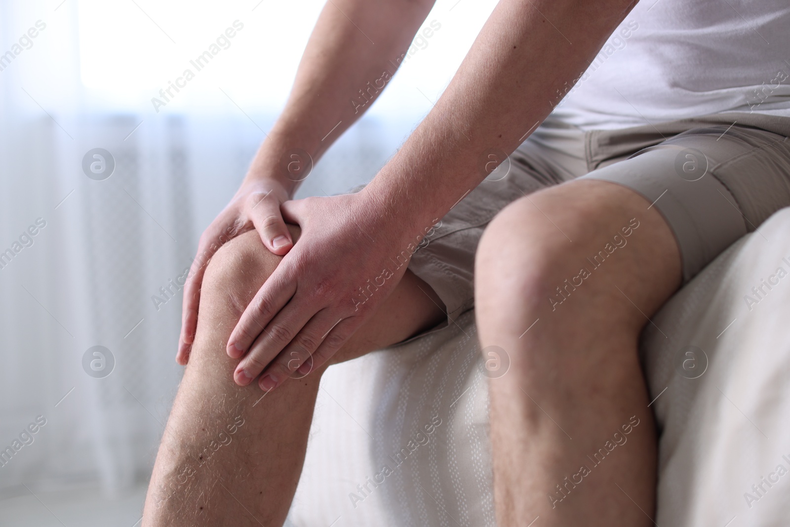 Man suffering from knee pain on bed at home, closeup Photo of Man suffering from knee pain on bed at home, closeup