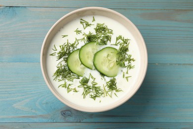 Photo of Tasty cucumber soup in bowl with dill on light blue wooden table, top view