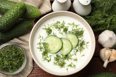 Photo of Tasty cucumber soup in bowl and ingredients on wooden table, flat lay