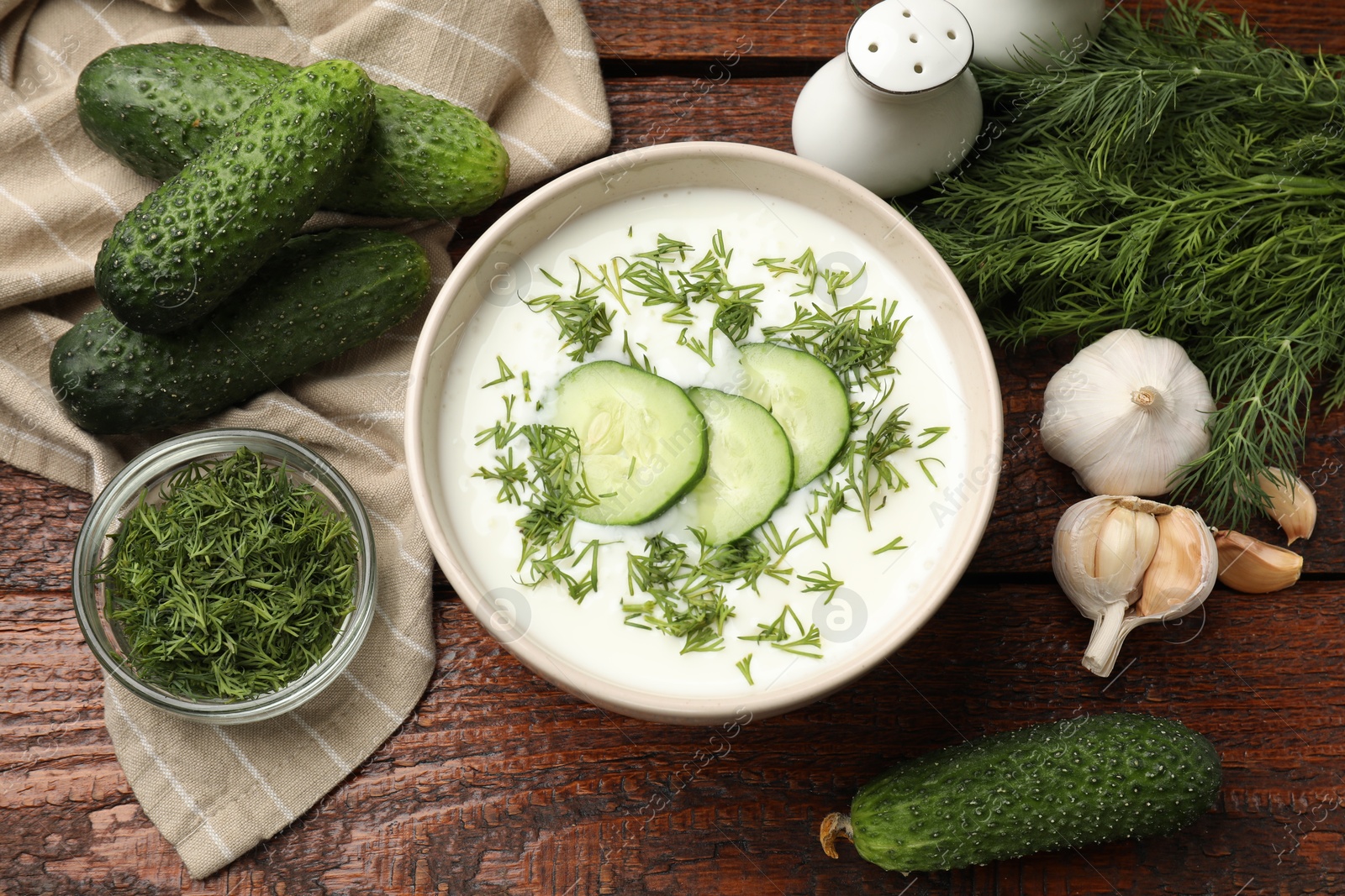 Tasty cucumber soup in bowl and ingredients on wooden table, flat lay Photo of Tasty cucumber soup in bowl and ingredients on wooden table, flat lay