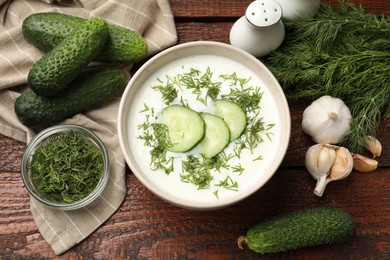 Photo of Tasty cucumber soup in bowl and ingredients on wooden table, flat lay