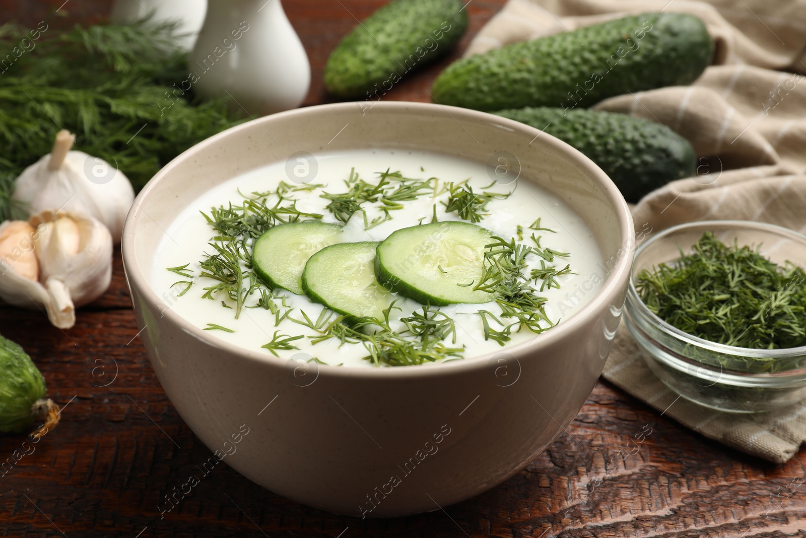 Tasty cucumber soup in bowl and ingredients on wooden table, closeup Photo of Tasty cucumber soup in bowl and ingredients on wooden table, closeup