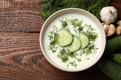 Photo of Tasty cucumber soup in bowl and ingredients on wooden table, flat lay. Space for text
