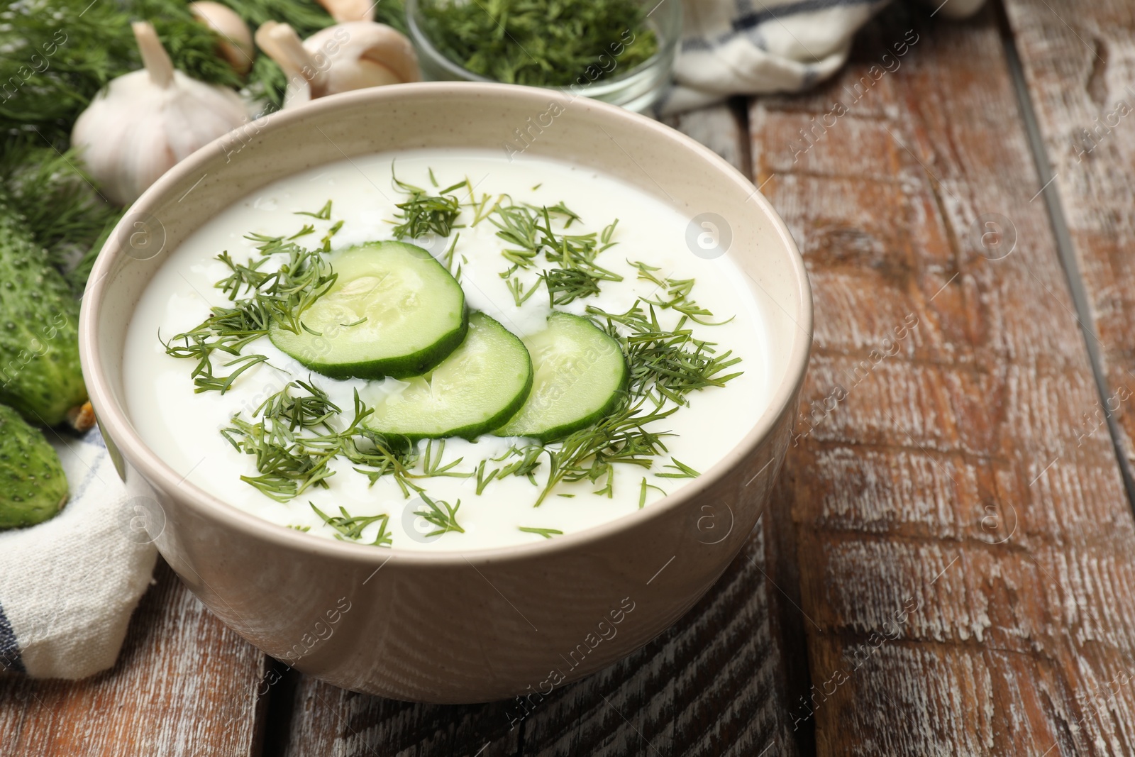 Tasty cucumber soup in bowl and ingredients on wooden table, closeup Photo of Tasty cucumber soup in bowl and ingredients on wooden table, closeup
