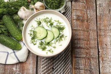 Photo of Tasty cucumber soup in bowl and ingredients on wooden table, flat lay. Space for text