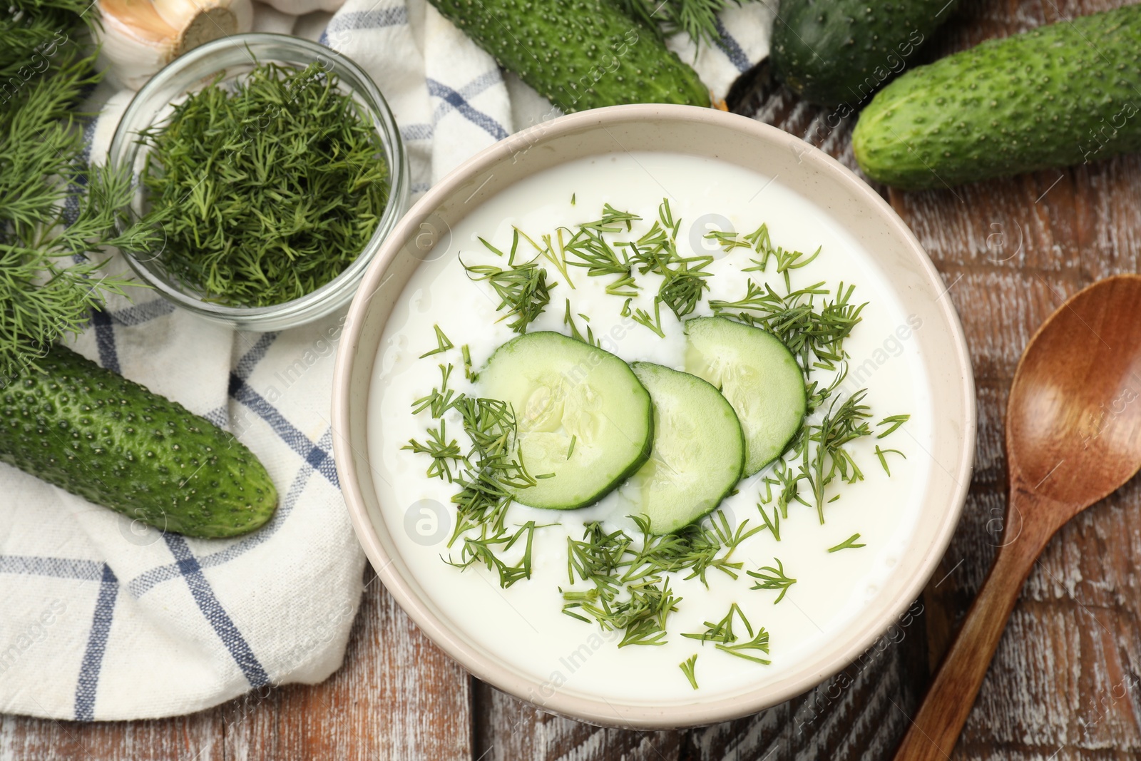 Tasty cucumber soup in bowl and ingredients on wooden table, flat lay Photo of Tasty cucumber soup in bowl and ingredients on wooden table, flat lay