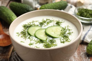 Photo of Tasty cucumber soup in bowl and ingredients on wooden table, closeup