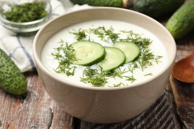 Photo of Tasty cucumber soup in bowl and ingredients on wooden table, closeup