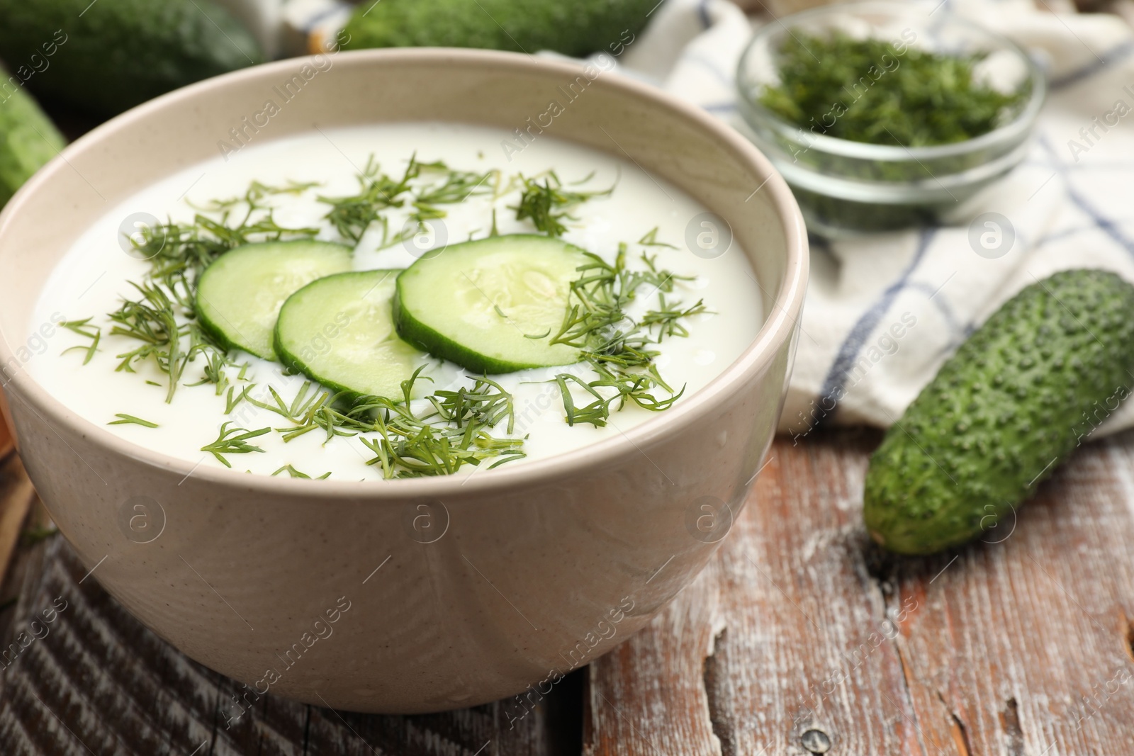 Tasty cucumber soup in bowl and ingredients on wooden table, closeup Photo of Tasty cucumber soup in bowl and ingredients on wooden table, closeup