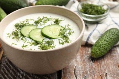 Photo of Tasty cucumber soup in bowl and ingredients on wooden table, closeup
