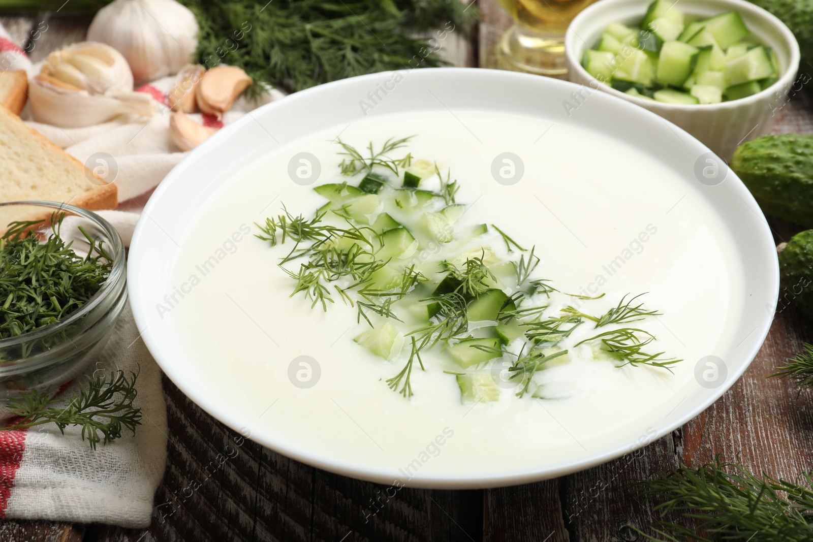 Tasty cucumber soup in bowl and ingredients on wooden table, closeup Photo of Tasty cucumber soup in bowl and ingredients on wooden table, closeup