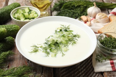 Photo of Tasty cucumber soup in bowl and ingredients on wooden table, closeup