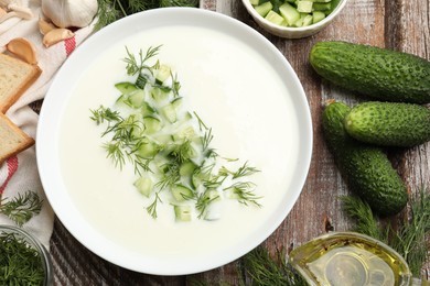 Photo of Tasty cucumber soup in bowl and ingredients on wooden table, flat lay