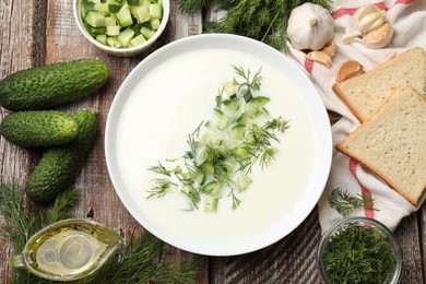 Photo of Tasty cucumber soup in bowl and ingredients on wooden table, flat lay