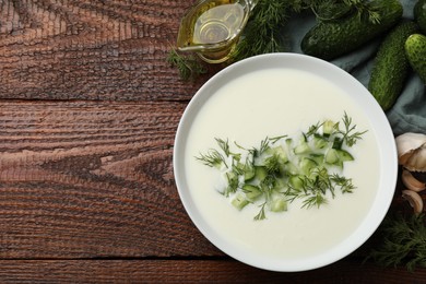 Photo of Tasty cucumber soup in bowl and ingredients on wooden table, flat lay. Space for text