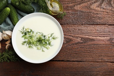 Photo of Tasty cucumber soup in bowl and ingredients on wooden table, flat lay. Space for text
