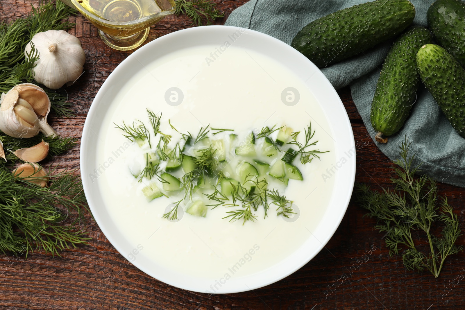Photo of Tasty cucumber soup in bowl and ingredients on wooden table, flat lay