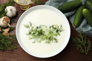 Photo of Tasty cucumber soup in bowl and ingredients on wooden table, flat lay