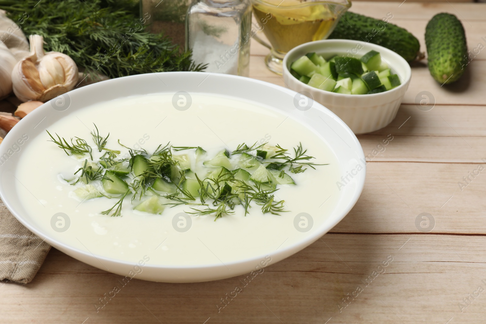 Tasty cucumber soup in bowl and ingredients on light wooden table, closeup Photo of Tasty cucumber soup in bowl and ingredients on light wooden table, closeup