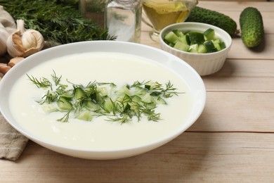 Photo of Tasty cucumber soup in bowl and ingredients on light wooden table, closeup