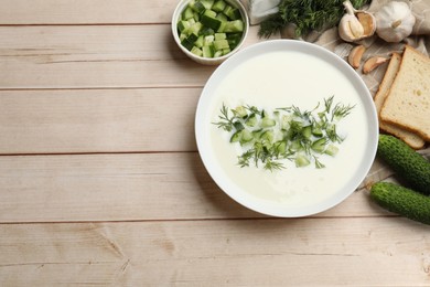 Photo of Tasty cucumber soup in bowl and ingredients on light wooden table, flat lay. Space for text