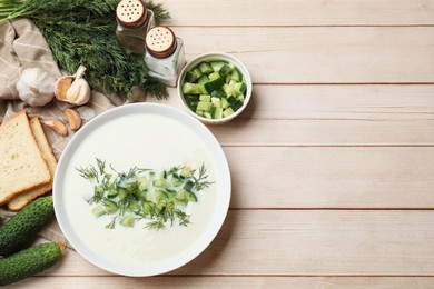 Photo of Tasty cucumber soup in bowl and ingredients on light wooden table, flat lay. Space for text