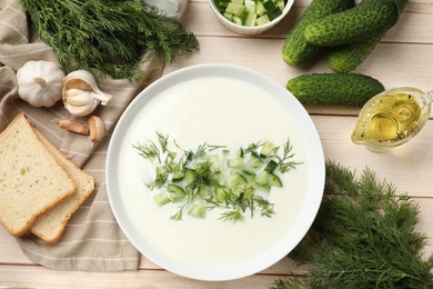 Photo of Tasty cucumber soup in bowl and ingredients on light wooden table, flat lay