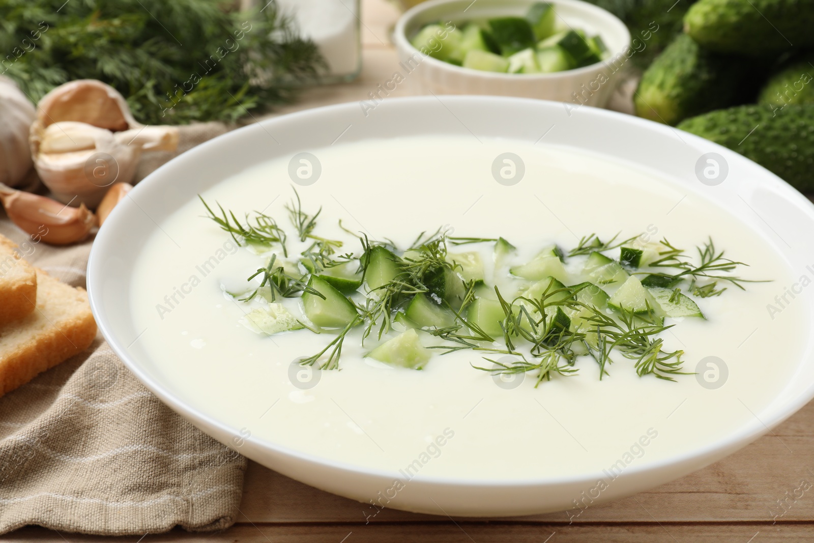 Tasty cucumber soup in bowl and ingredients on light wooden table, closeup Photo of Tasty cucumber soup in bowl and ingredients on light wooden table, closeup