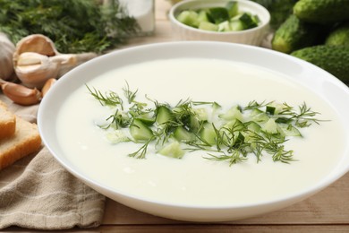 Photo of Tasty cucumber soup in bowl and ingredients on light wooden table, closeup