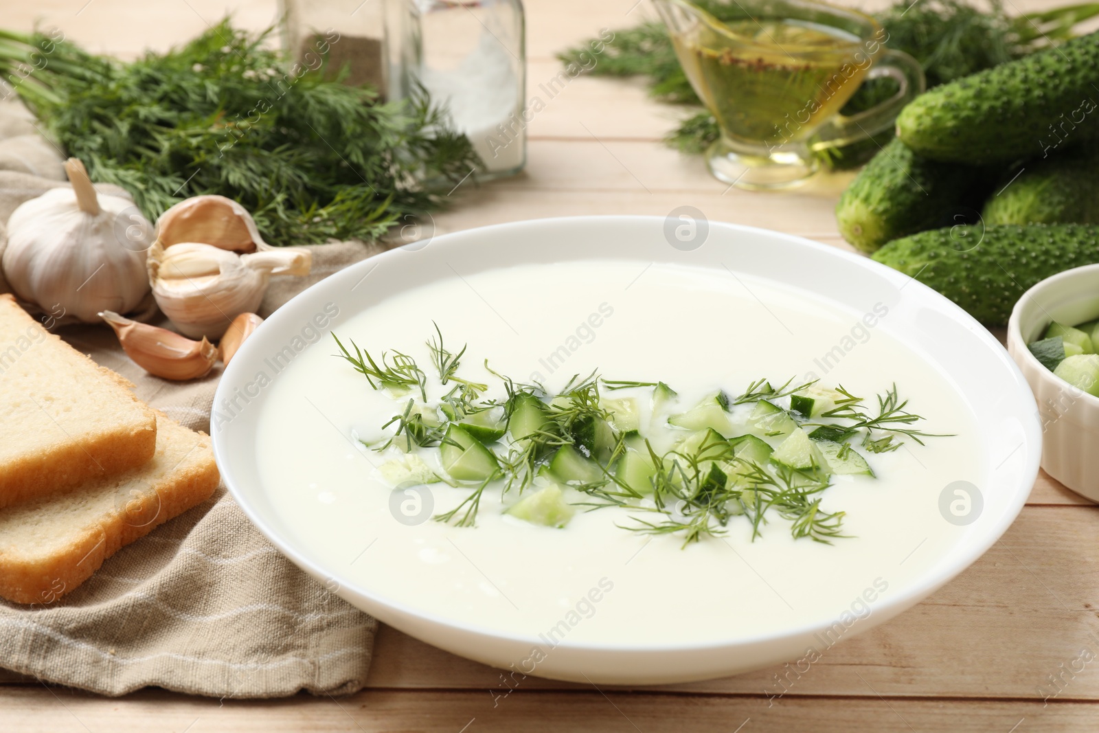 Tasty cucumber soup in bowl and ingredients on light wooden table, closeup Photo of Tasty cucumber soup in bowl and ingredients on light wooden table, closeup