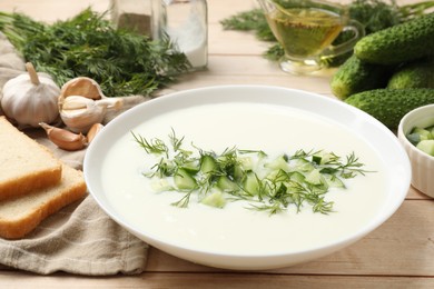 Photo of Tasty cucumber soup in bowl and ingredients on light wooden table, closeup