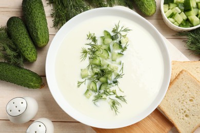 Photo of Tasty cucumber soup in bowl and ingredients on light wooden table, flat lay