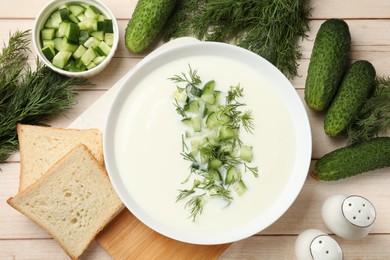 Photo of Tasty cucumber soup in bowl and ingredients on light wooden table, flat lay