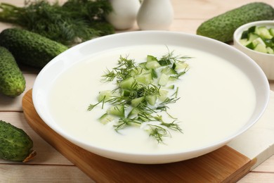 Photo of Tasty cucumber soup in bowl and ingredients on light wooden table, closeup