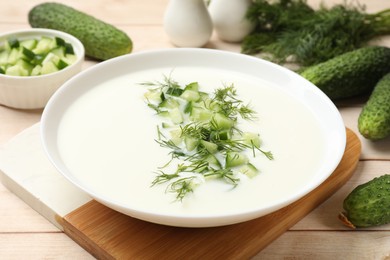 Photo of Tasty cucumber soup in bowl and ingredients on light wooden table, closeup