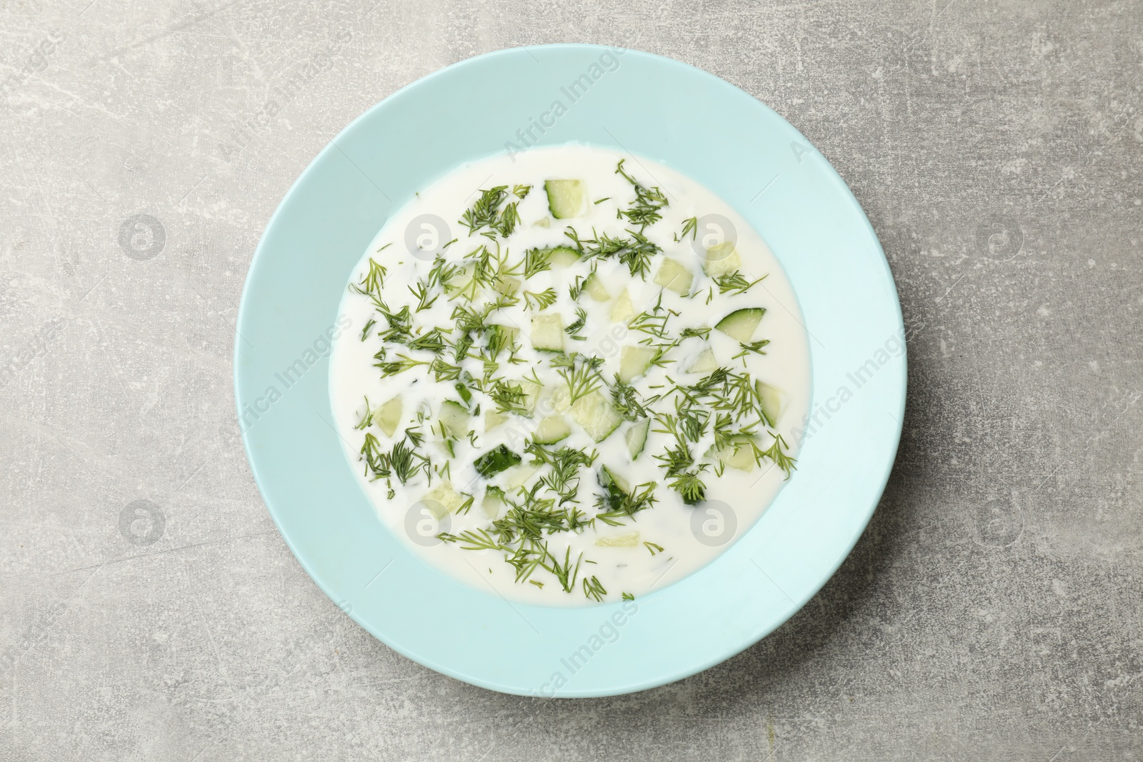 Tasty cucumber soup with dill on grey textured table, top view Photo of Tasty cucumber soup with dill on grey textured table, top view