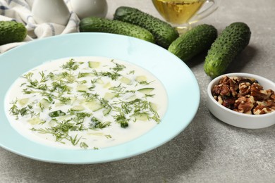 Photo of Tasty cucumber soup with dill and nuts on grey textured table, closeup