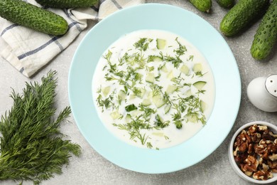 Photo of Tasty cucumber soup with dill and nuts on grey textured table, flat lay