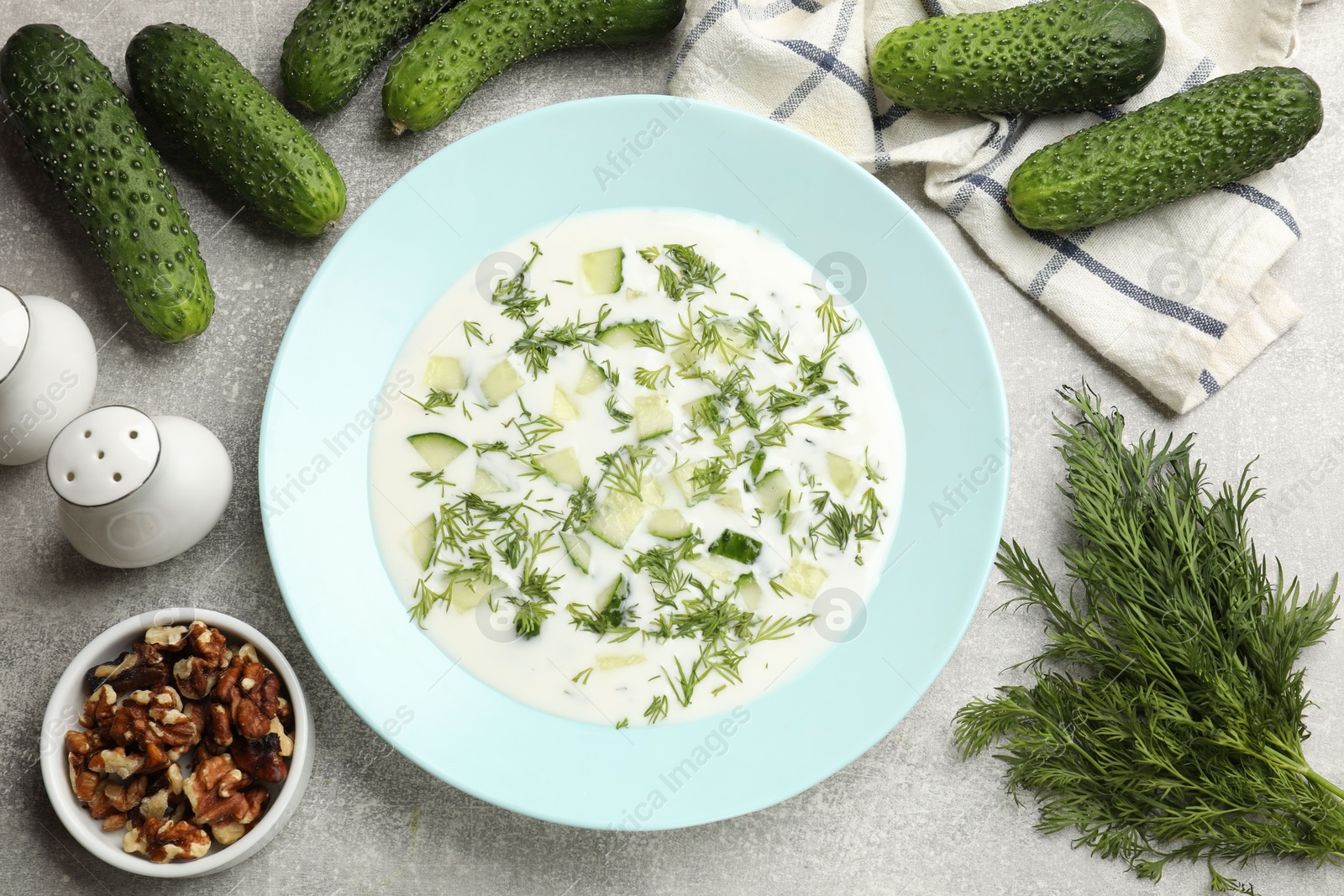 Tasty cucumber soup with dill and nuts on grey textured table, flat lay Photo of Tasty cucumber soup with dill and nuts on grey textured table, flat lay