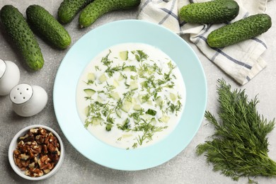 Photo of Tasty cucumber soup with dill and nuts on grey textured table, flat lay