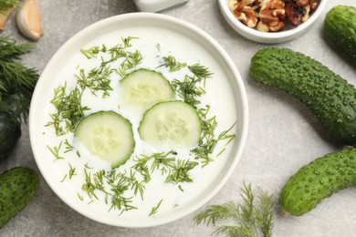 Photo of Tasty cucumber soup with dill in bowl and nuts on grey textured table, flat lay