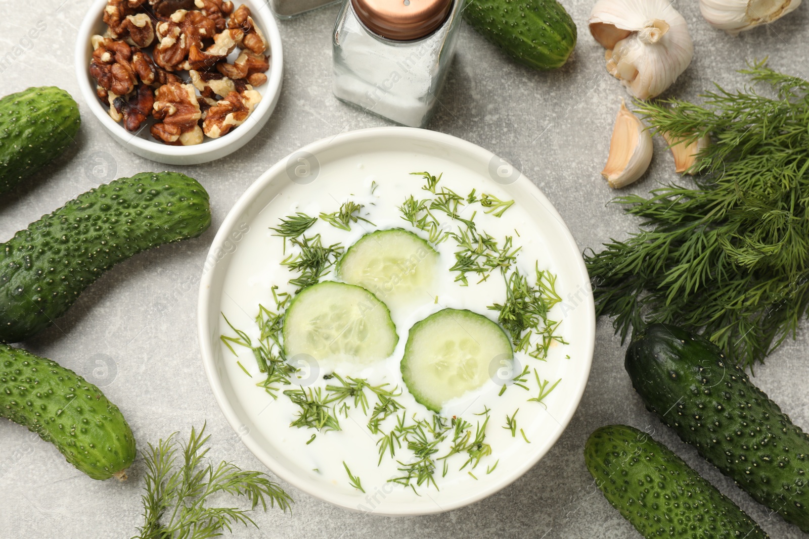 Tasty cucumber soup with dill in bowl and products on grey textured table, flat lay Photo of Tasty cucumber soup with dill in bowl and products on grey textured table, flat lay