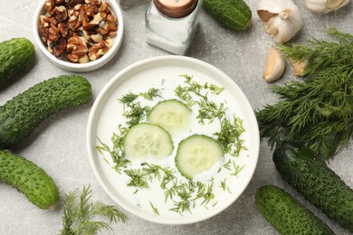 Photo of Tasty cucumber soup with dill in bowl and products on grey textured table, flat lay