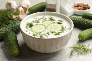 Photo of Tasty cucumber soup with dill in bowl on grey textured table, closeup