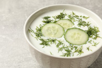 Photo of Tasty cucumber soup with dill in bowl on grey textured table, closeup