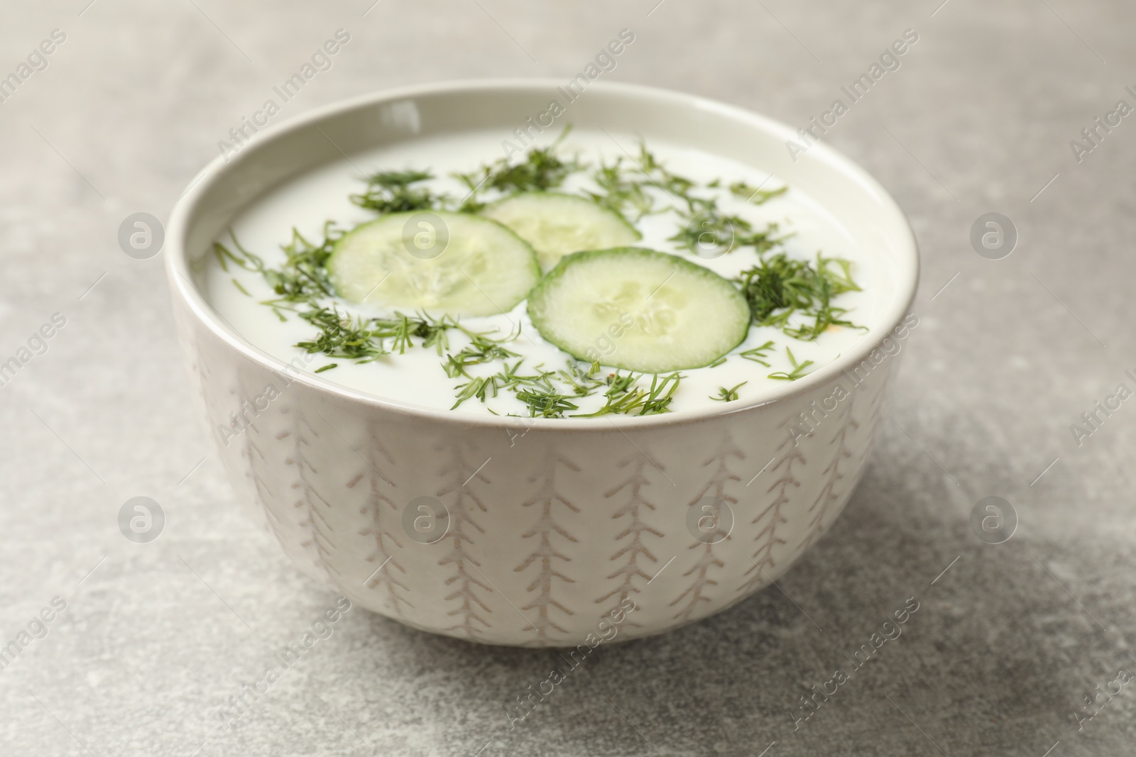Tasty cucumber soup with dill in bowl on grey textured table, closeup Photo of Tasty cucumber soup with dill in bowl on grey textured table, closeup