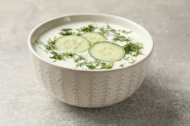 Photo of Tasty cucumber soup with dill in bowl on grey textured table, closeup