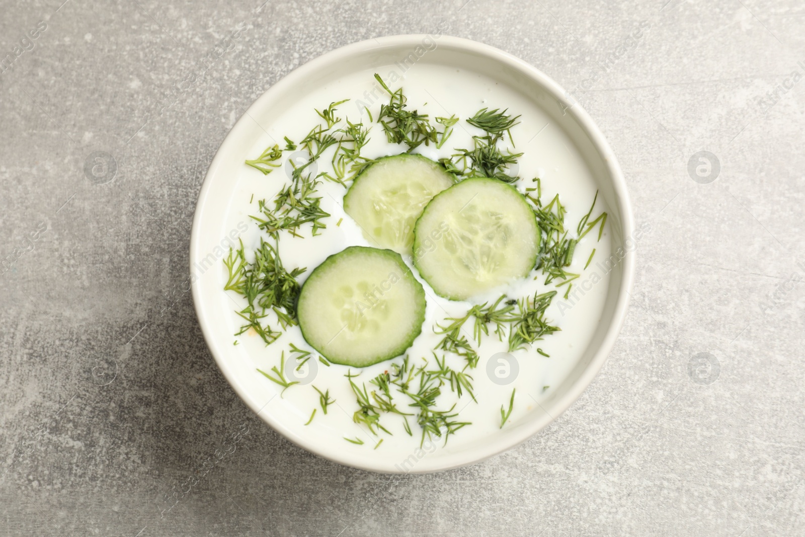Tasty cucumber soup with dill in bowl on grey textured table, top view Photo of Tasty cucumber soup with dill in bowl on grey textured table, top view