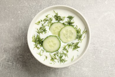 Photo of Tasty cucumber soup with dill in bowl on grey textured table, top view